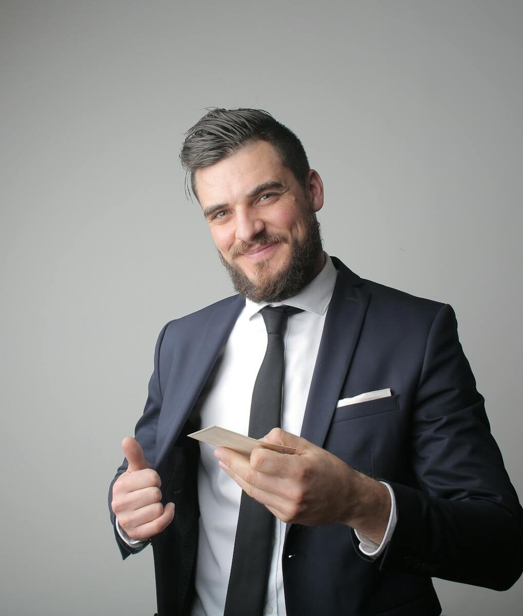 Smiling businessman in formal attire holding a card, exuding confidence in a studio portrait.